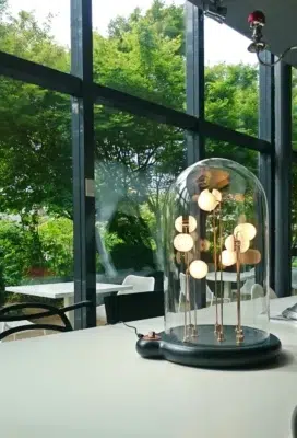 Germes de Lux luminous artwork glowing softly under glass dome on a table with garden view