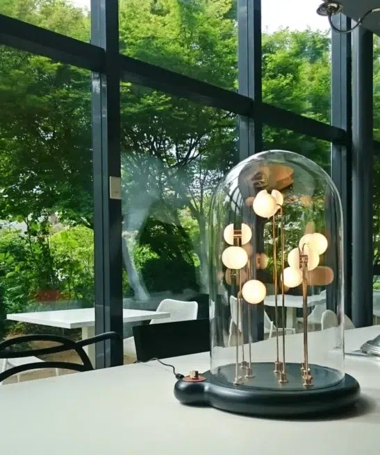Germes de Lux luminous artwork glowing softly under glass dome on a table with garden view