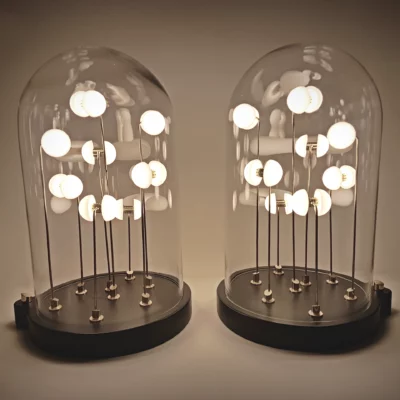 Two Germes de Lux light sculptures side by side, glowing warmly under glass domes