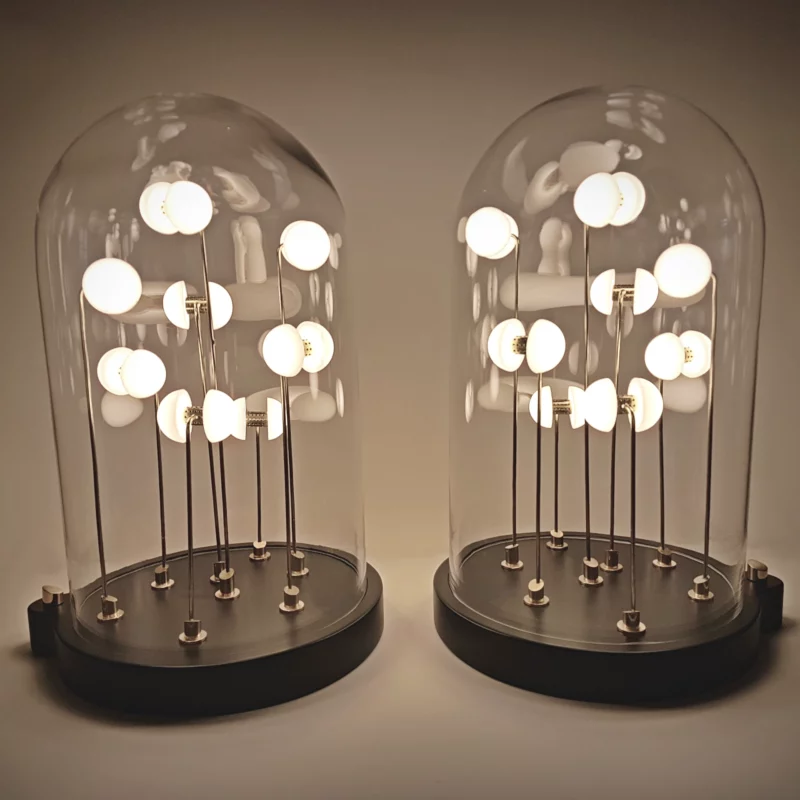 Two Germes de Lux light sculptures side by side, glowing warmly under glass domes