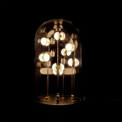 Germes de Lux luminous artwork under a glass dome, glowing warmly in darkness