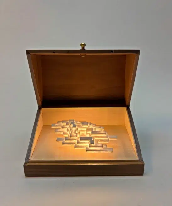 Open walnut box showing the white plaster sculpture of Vapor Minimus illuminated inside.