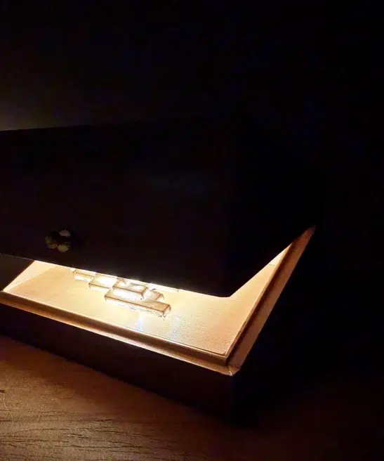 Vapor Minimus glowing inside an open walnut box in the dark.